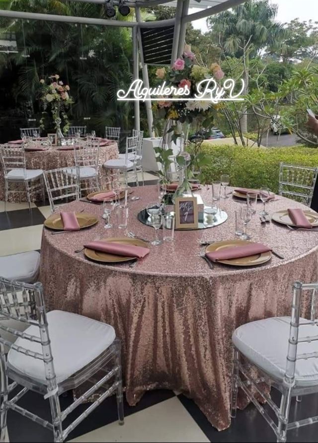 Mesa redonda con mantel de lentejuelas rosa dorado y sillas transparentes