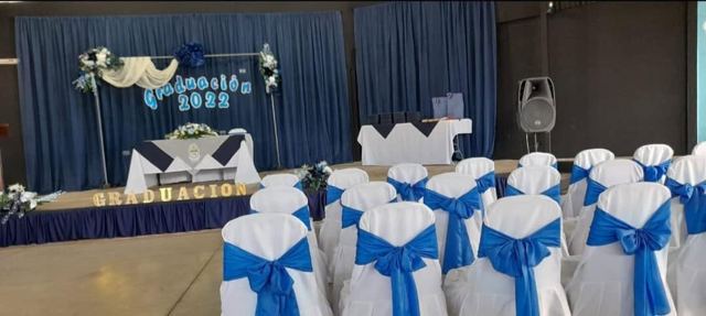 Sillas forradas blancas con lazo azul frente a escenario