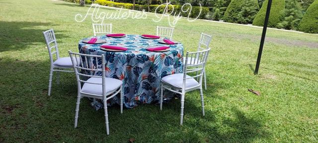 Mesa redonda con mantel floral y sillas Tiffany blancas en jardín