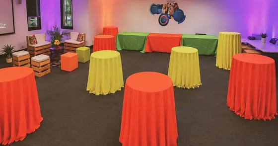 Salón con mesas cocteleras forradas en naranja y amarillo y sala lounge de tarimas para un festival