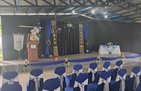 Ceremonia de graduación con filas de sillas cubiertas en azul y lazos plateados