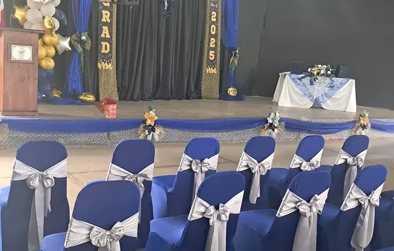 Graduación con sillas cubiertas en azul y lazos plateados frente a la tarima