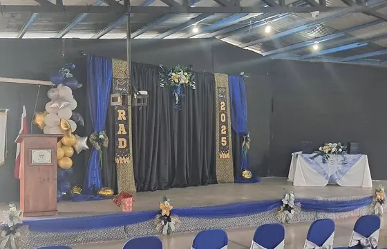 Tarima de graduación decorada con globos, cortinas azules y mesa principal