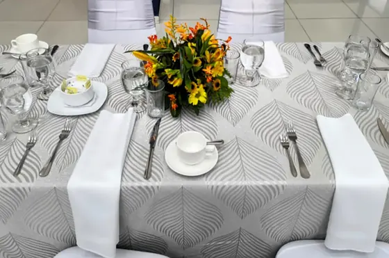 Mesa con mantelería de lujo gris con diseño de hojas y servilletas blancas