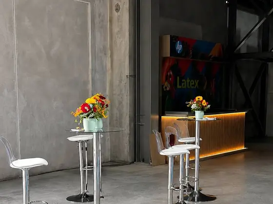 Mesas cocteleras de vidrio con sillas altas blancas en una bodega para un evento de empresa