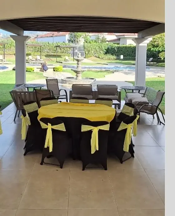 Mesa redonda con mantel amarillo y sillas con cobertor negro y lazo amarillo en una terraza